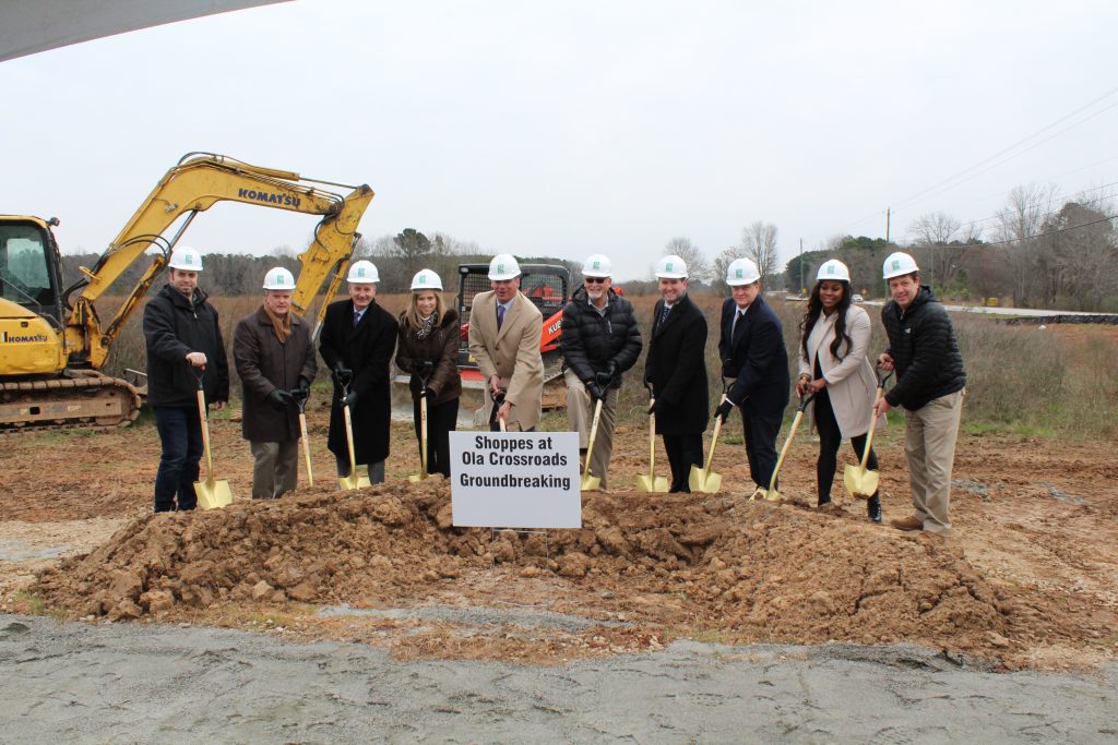 people in hard hats with shovels turning dirt with construction equipment behind them